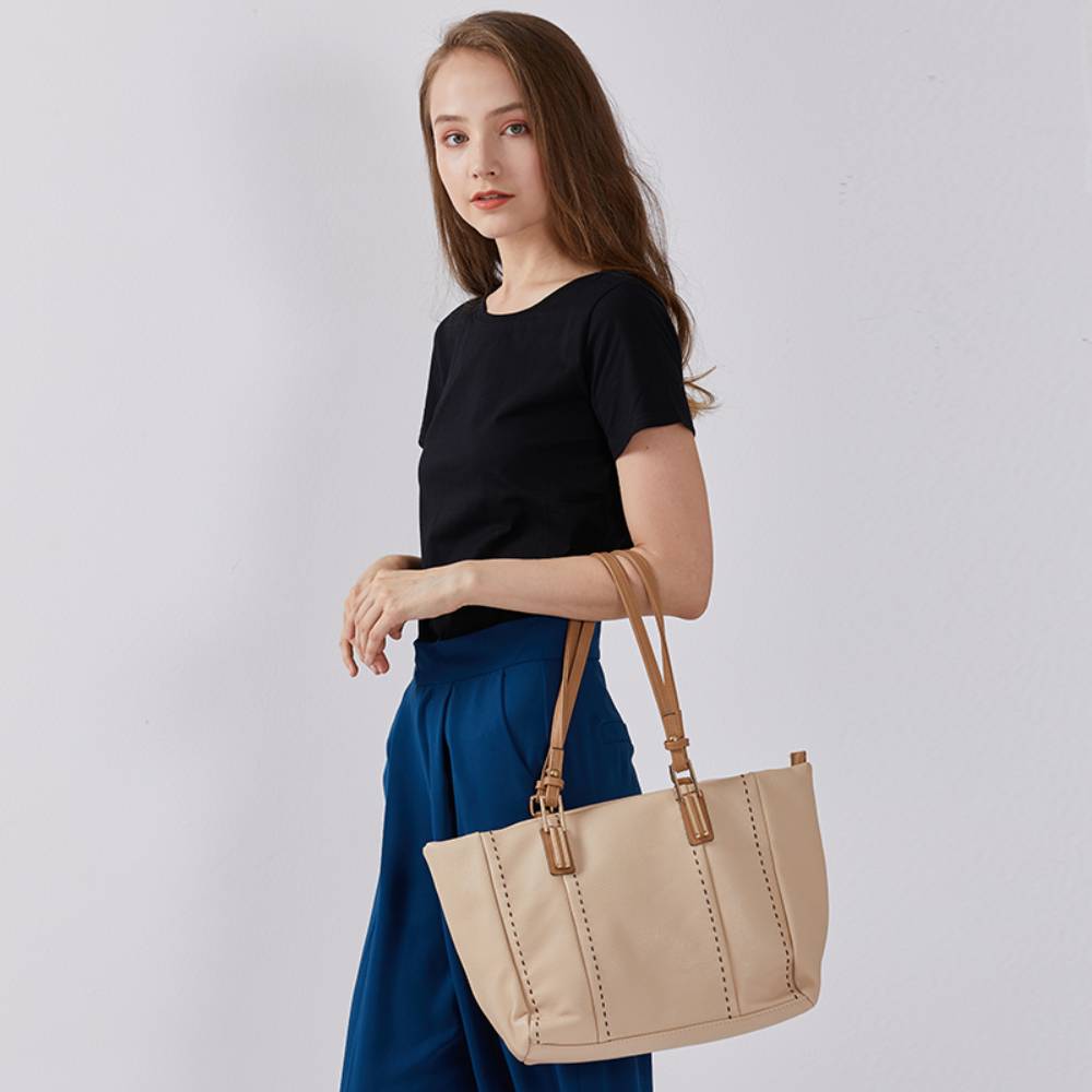 Model carrying a beige/white large tote bag with brown leather handles, casual everyday fashion for work and commute.
