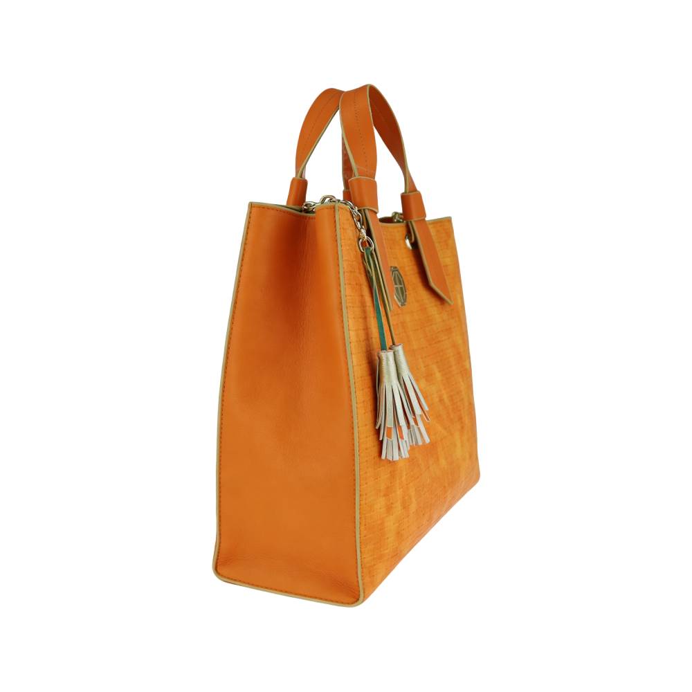 Side view of orange woven tote bag with leather trim and silver tassels, showing spacious capacity and durable construction.