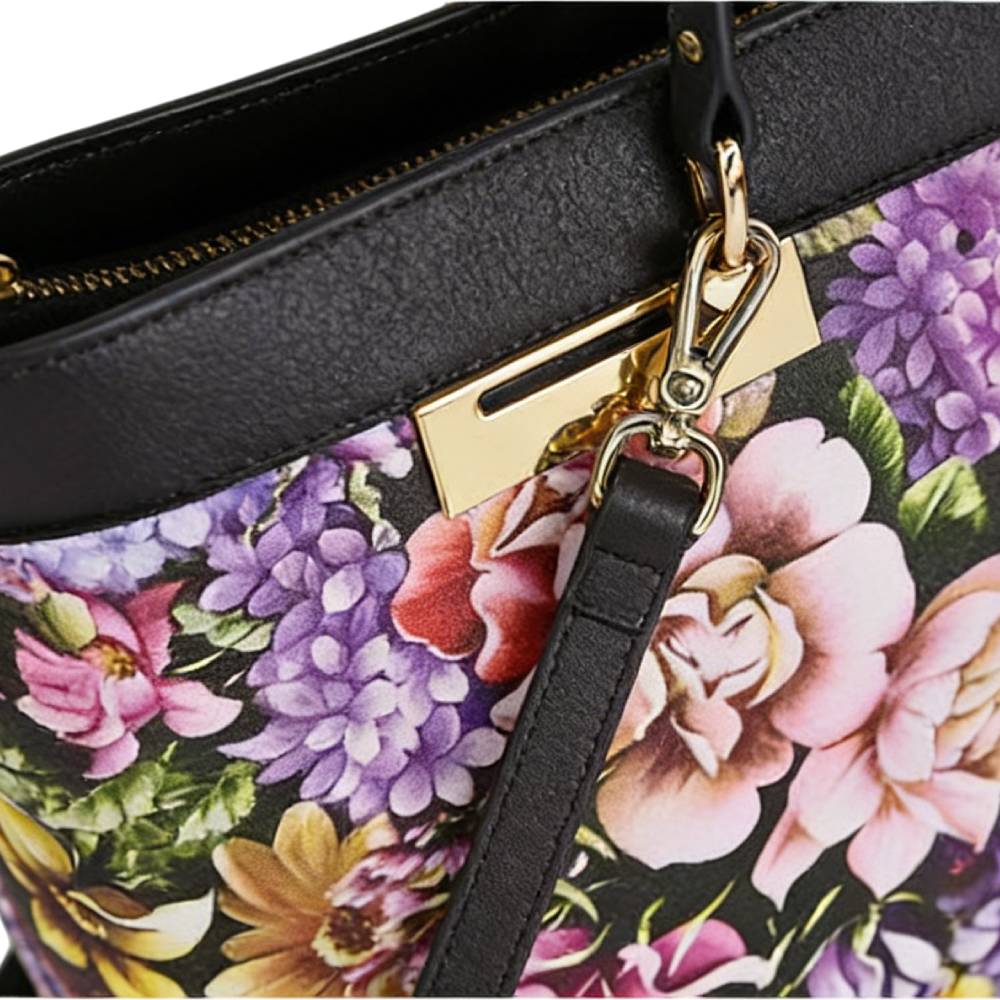 Close-up of gold metal hardware and black leather strap attachment on floral tote bag, highlighting sturdy craftsmanship.
