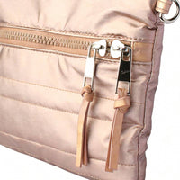 Close-up of rose gold quilted crossbody bag’s front zipper, showcasing silver metal pulls with leather tassel accents and precise horizontal stitching.
