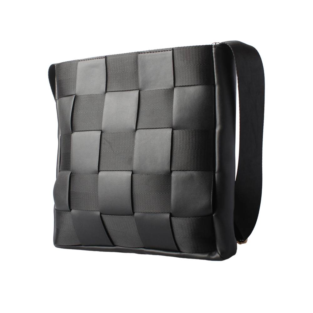 Side view of a black woven crossbody bag, displaying a checkered pattern of leather and webbing straps, emphasizing modern texture and durability.