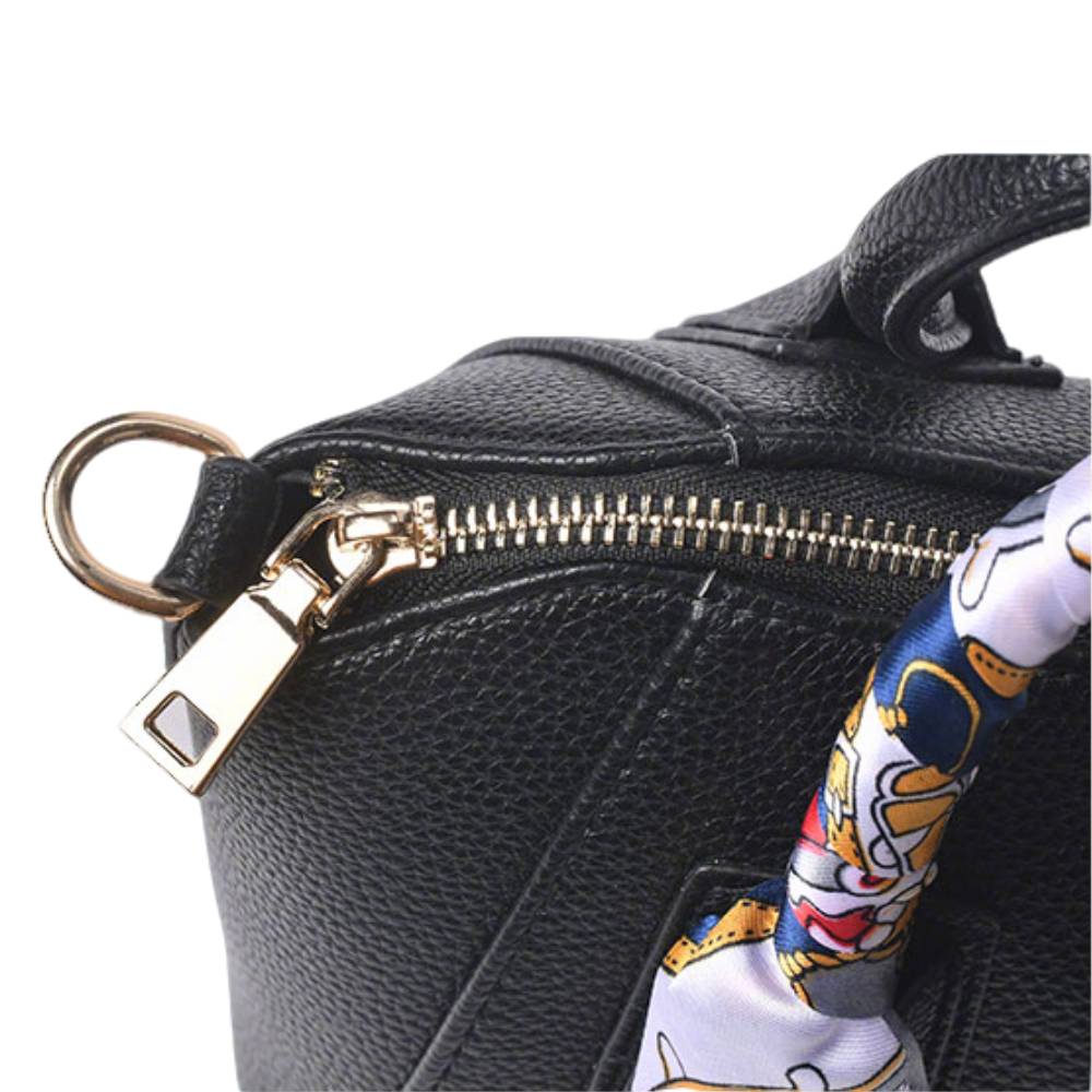 Close-up of gold metal hardware (zipper pull and D-ring) on a black pebbled leather handbag, highlighting premium craftsmanship and durable construction.