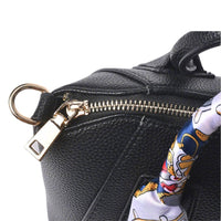 Close-up of gold metal hardware (zipper pull and D-ring) on a black pebbled leather handbag, highlighting premium craftsmanship and durable construction.