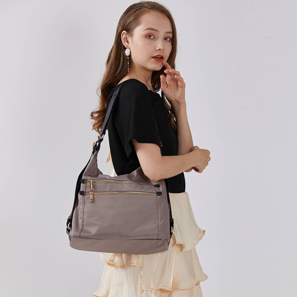 Model carrying a lightweight gray nylon shoulder bag with dual front zipper pockets, versatile casual style for commute and daily use.