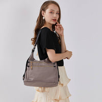 Model carrying a lightweight gray nylon shoulder bag with dual front zipper pockets, versatile casual style for commute and daily use.