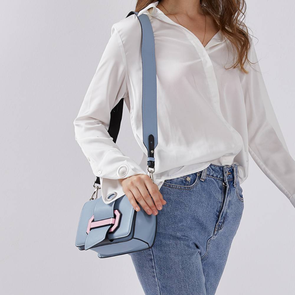Model holding a small light blue shoulder bag with pink accent buckle, minimalist design for women’s fashion.