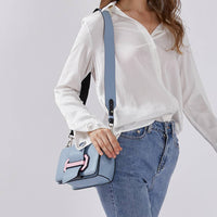 Model holding a small light blue shoulder bag with pink accent buckle, minimalist design for women’s fashion.