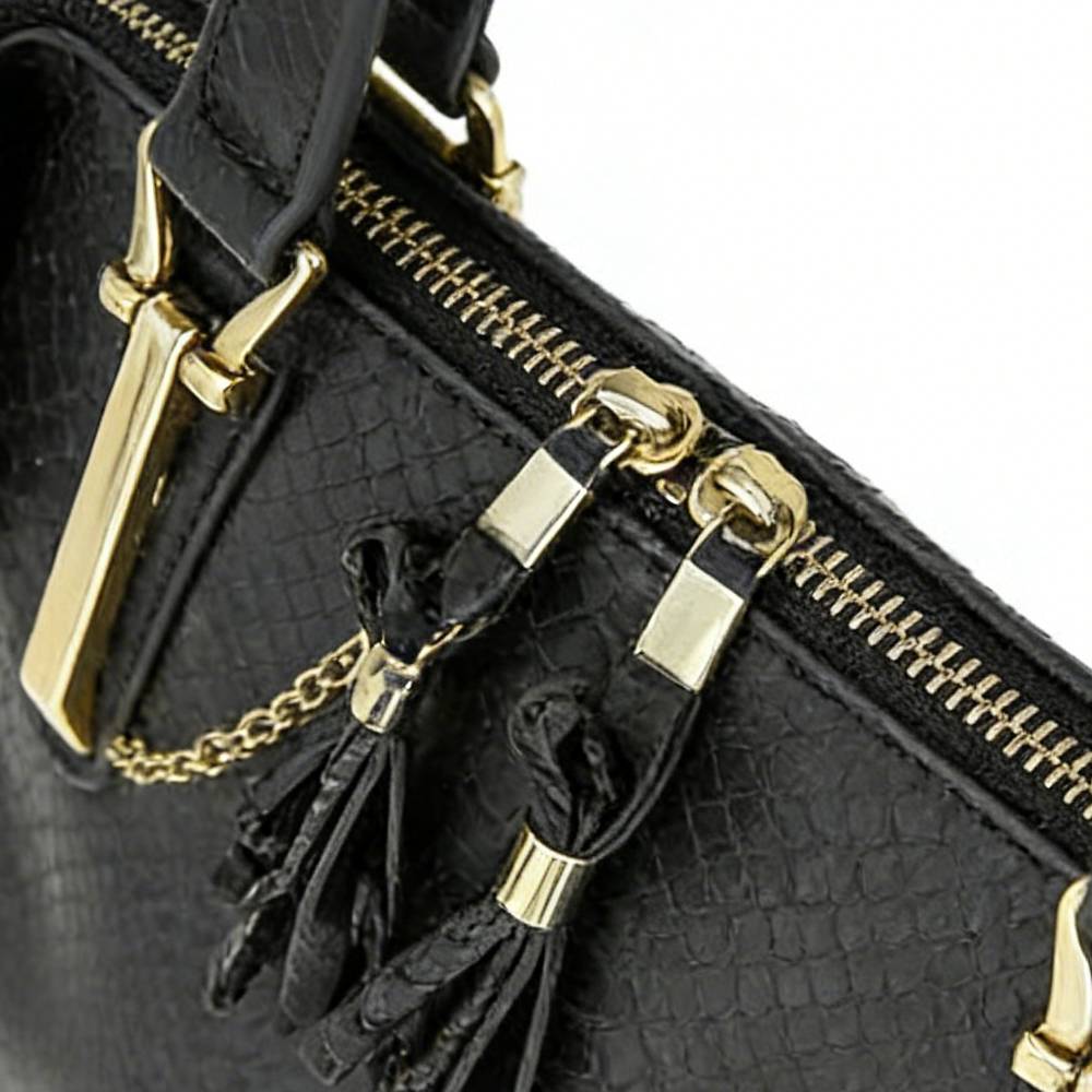 Close-up of black leather tassels with gold accents and chain detail on the zipper pull, showcasing decorative design.