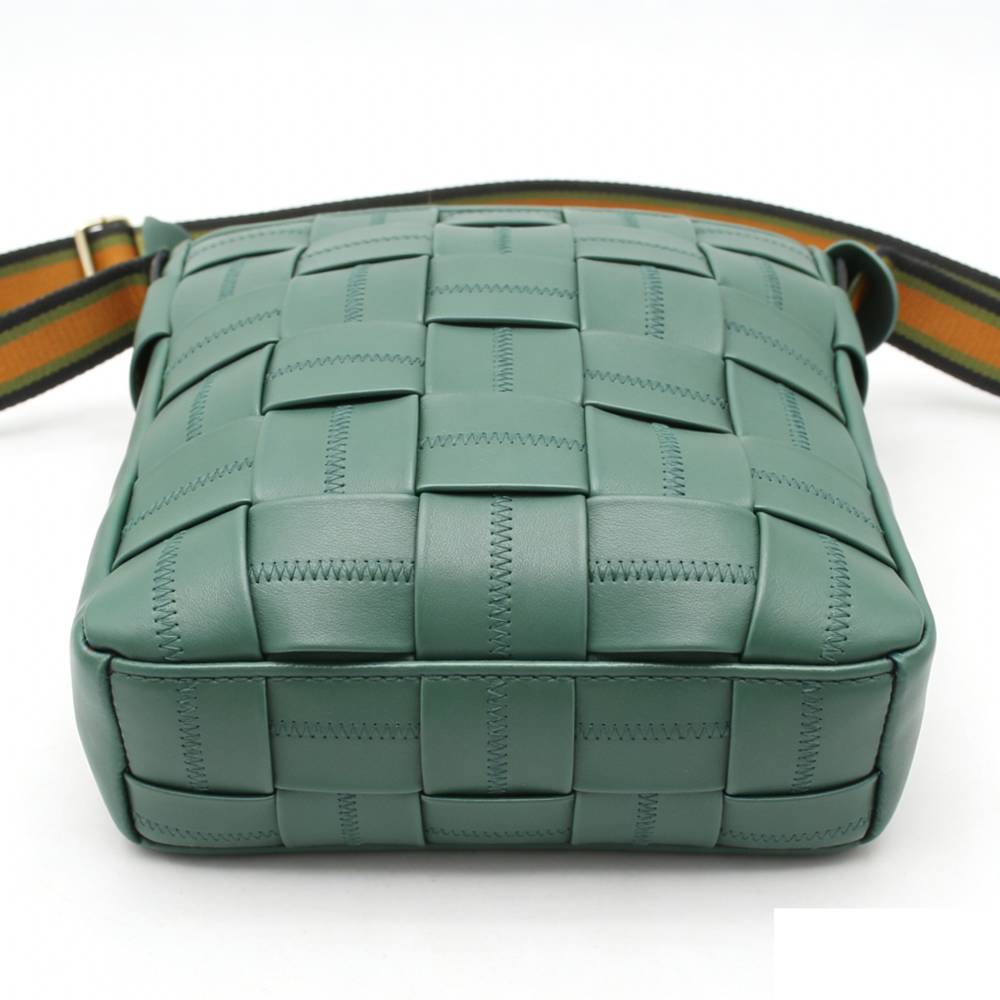 Bottom view of a teal woven leather crossbody bag, highlighting the detailed checkered woven pattern and reinforced base stitching.