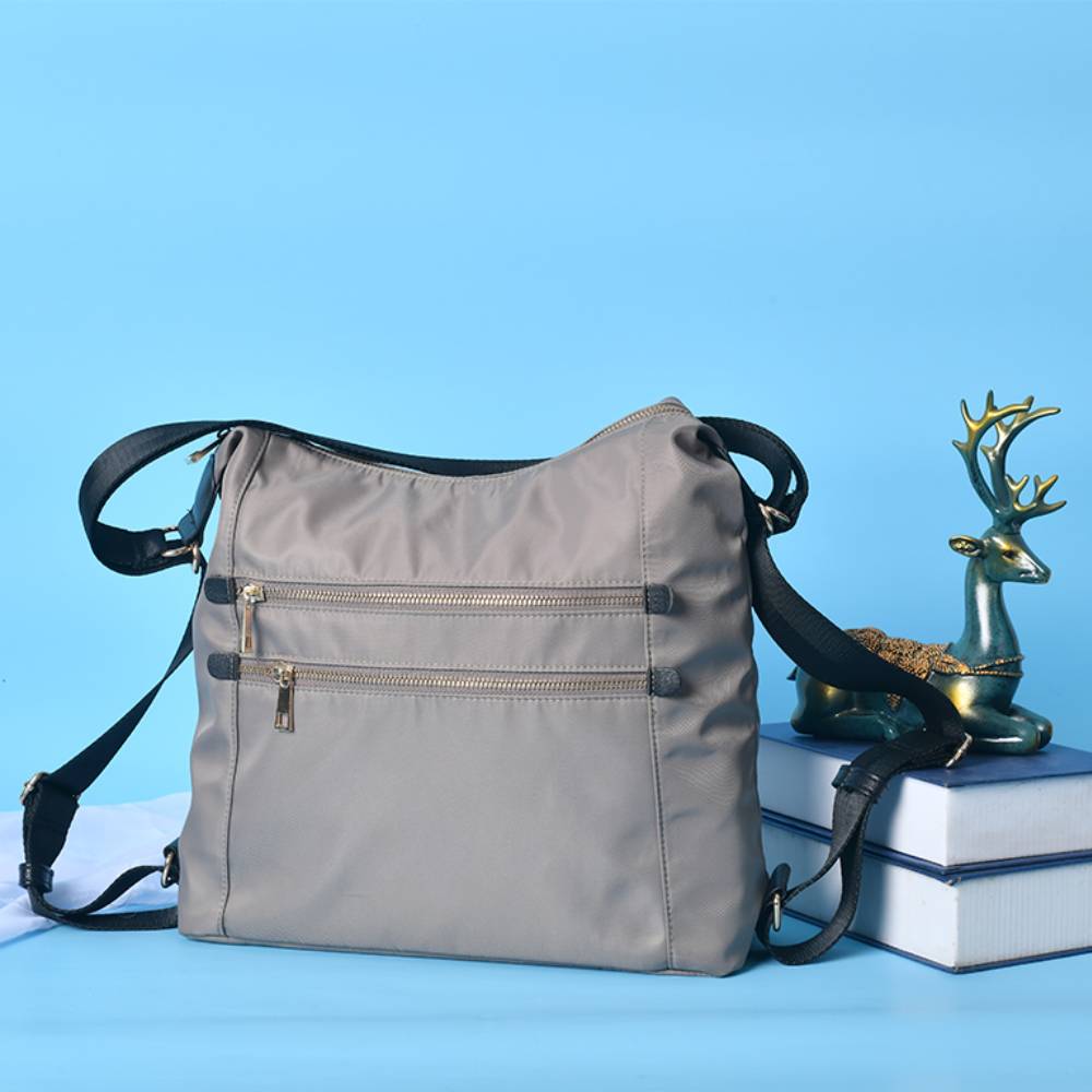 Gray nylon crossbody bag styled on a stack of books, minimalist casual design for wholesale and everyday fashion.