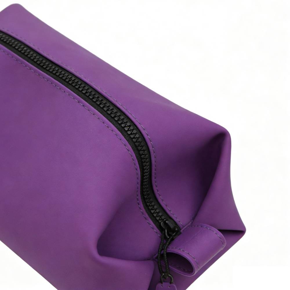 Close-up of purple toiletry bag with black rubberized zipper and contrast stitching, showcasing premium material quality and durable hardware details.